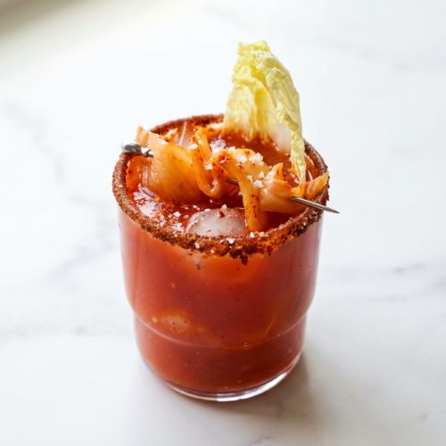 Mocktail au kimchi pétillant avec jus de citron vert frais et sel de mer, garni de tranches de lime et d'épices fermentées