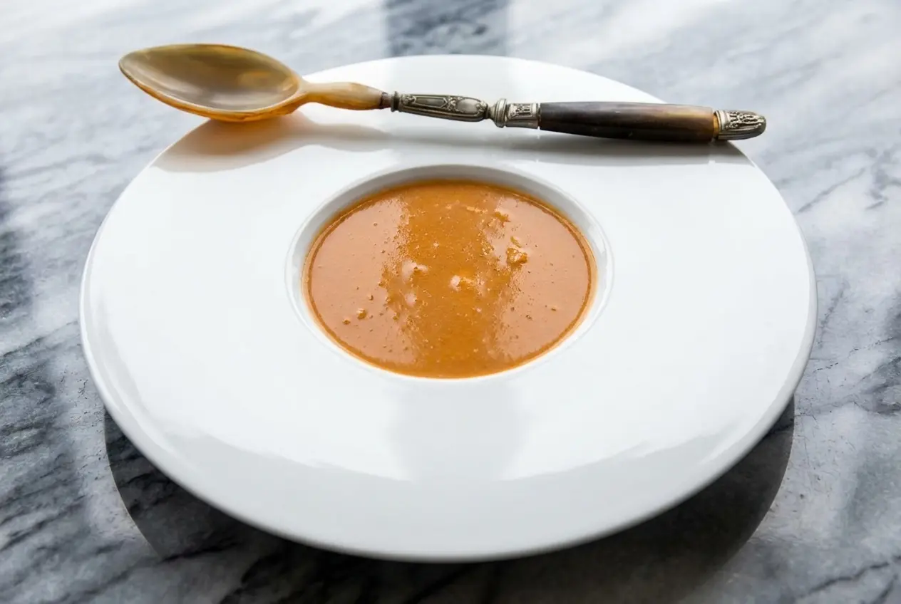 Assiette creuse avec la recette bisque de homard onctueuse, parfumée au Noilly Prat et à une étoile de badiane.