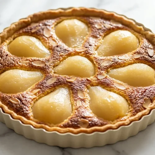 Tarte amandine aux poires dorée avec crème d'amande torréfiée au beurre noisette et poires tranchées sur une pâte sablée.